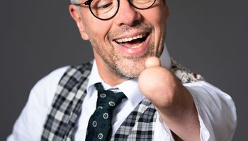 Rainer Schmidt streckt einen verkürzten Unterarm ohne Hand aus und schaut lächelnd auf seinen Daumen. Es ist der einzige Finger an seinem Arm.
